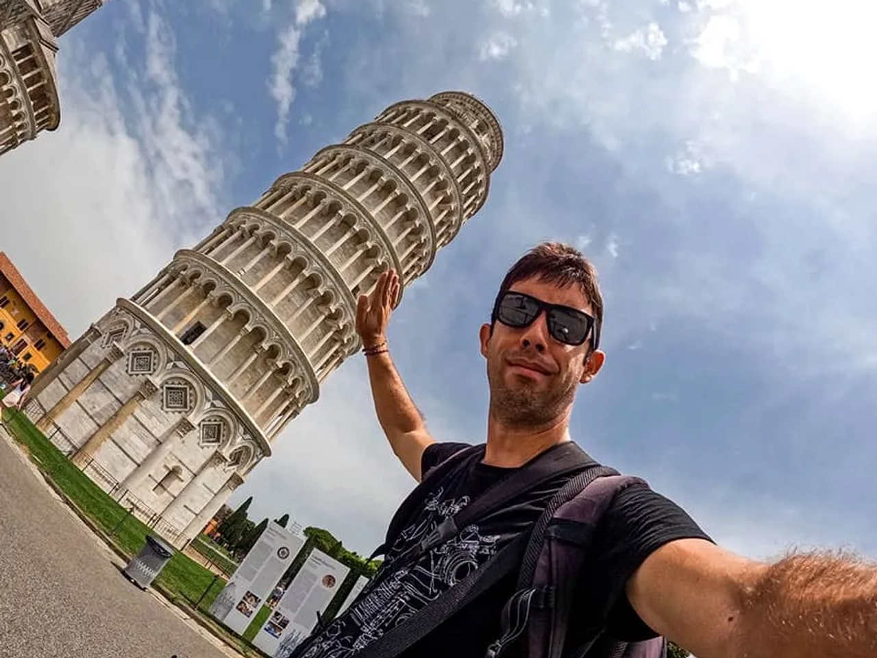 Hombre sosteniendo la Torre de Pisa con una mano, fondo de cielo nublado.