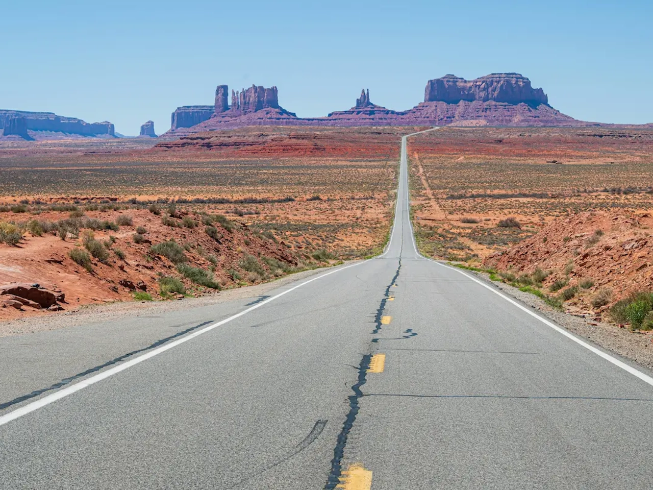 Carretera recta hacia Monument Valley con formaciones rocosas rojizas al fondo