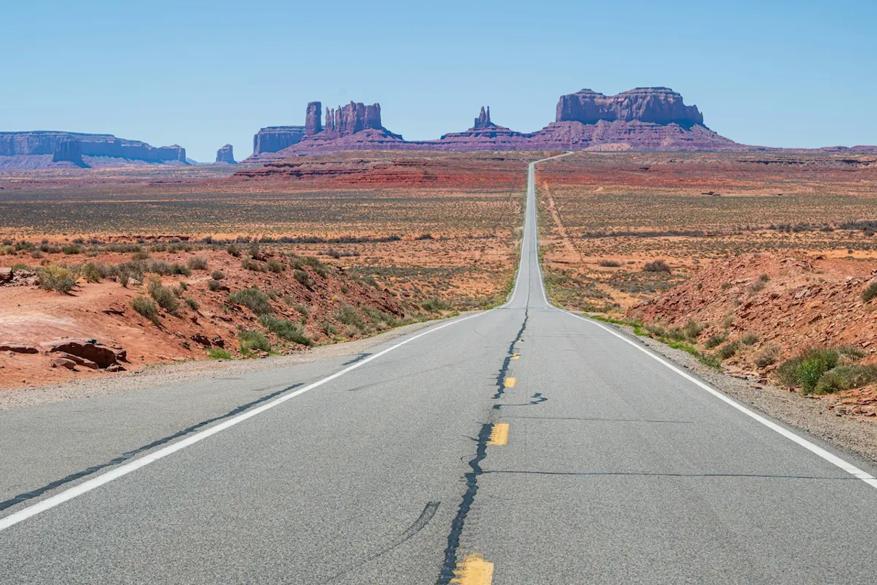 Carretera recta hacia Monument Valley con formaciones rocosas rojizas al fondo