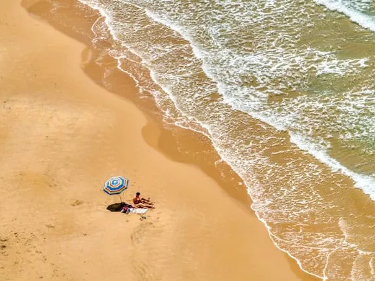 duas pessoas estendidas na areia junto a um guarda sol numa praia em Agrigento na sicilia
