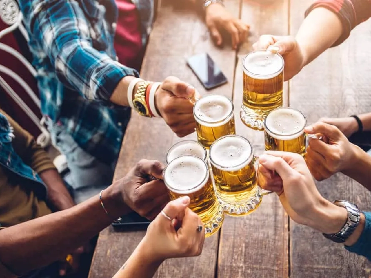 varios jovens a segurar canecas de cerveja sobre mesa de madeira