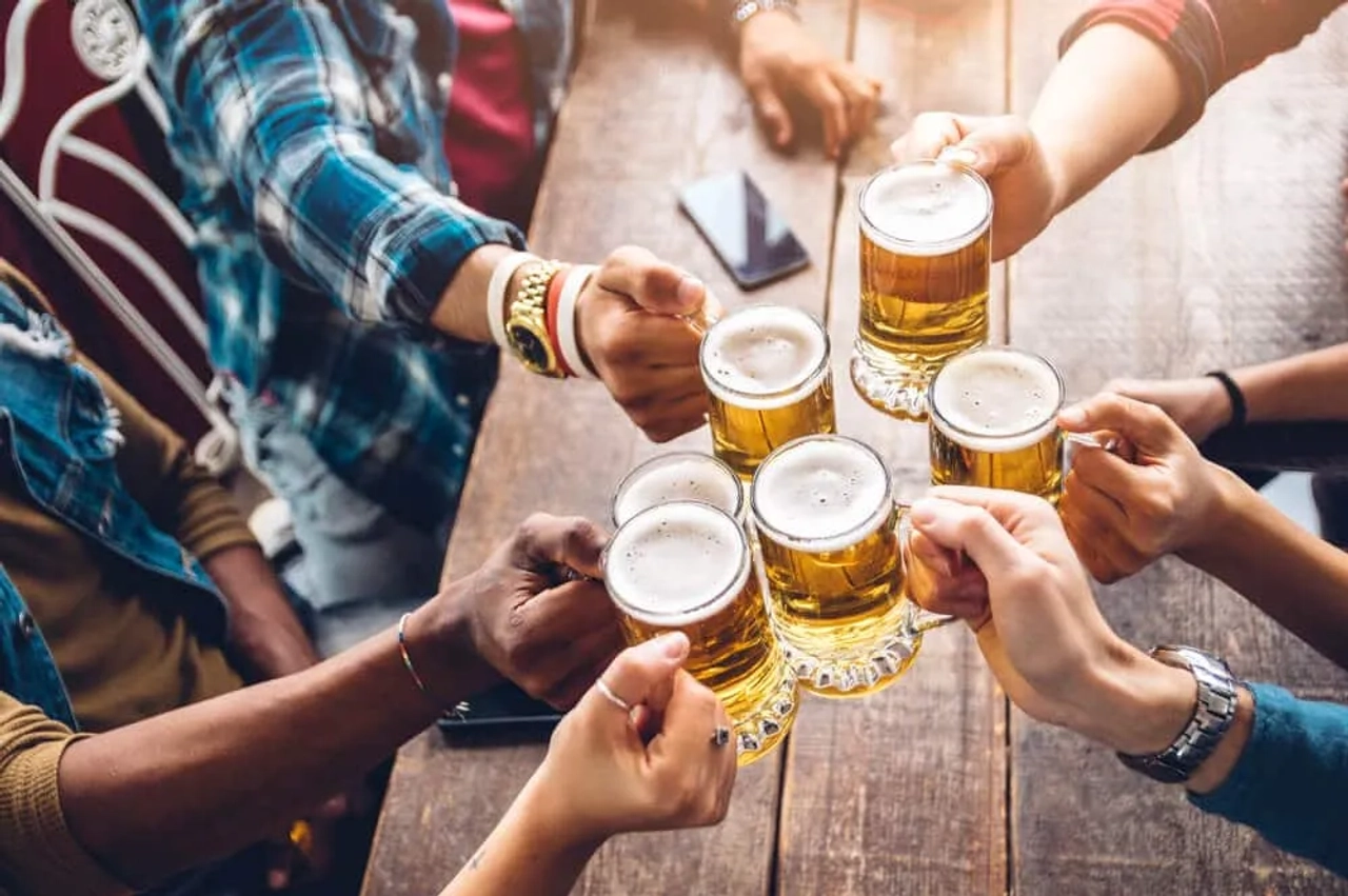 varios jovens a segurar canecas de cerveja sobre mesa de madeira