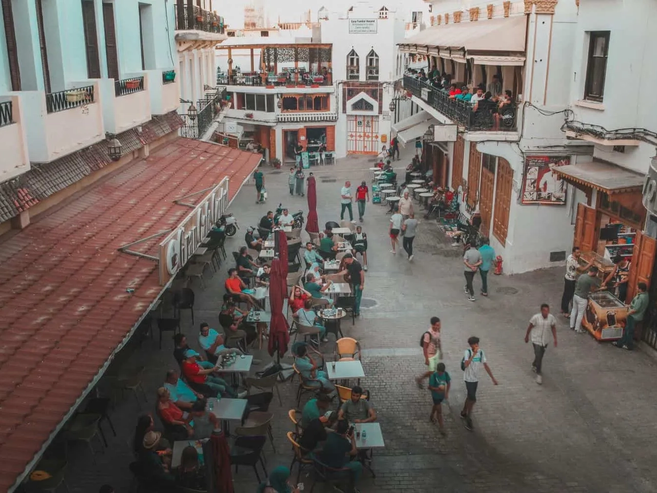 Praça movimentada em Tânger, com pessoas em cafés e lojas ao redor.
