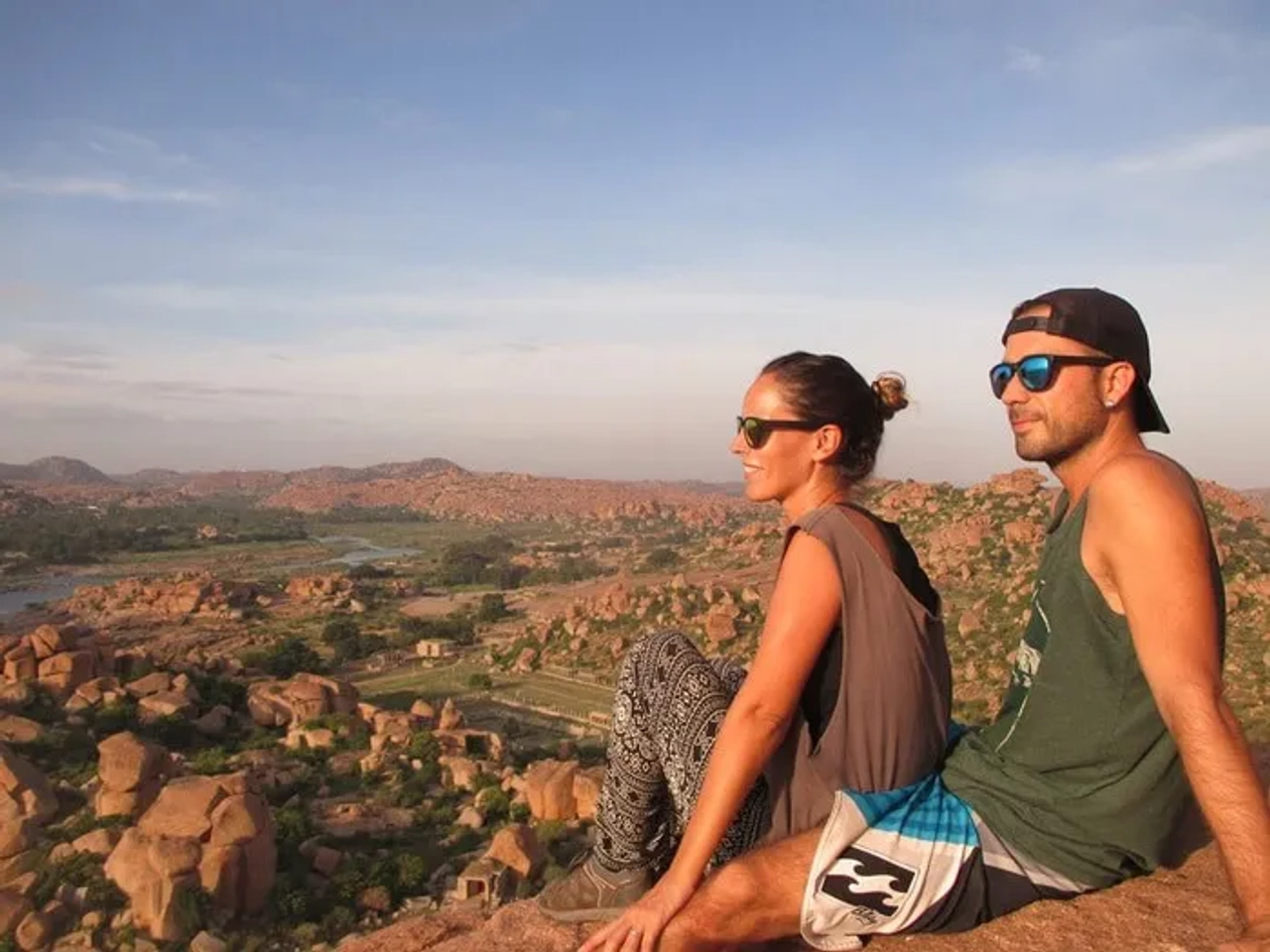 Pareja sentada en una roca, disfrutando de un paisaje montañoso al atardecer.