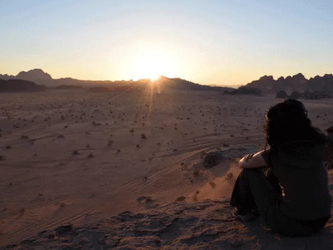 Mujer contemplando un amanecer en un desierto montañoso.