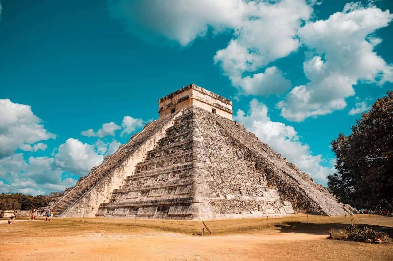 Pirâmide de Chichén Itzá sob céu azul, com visitantes ao redor.