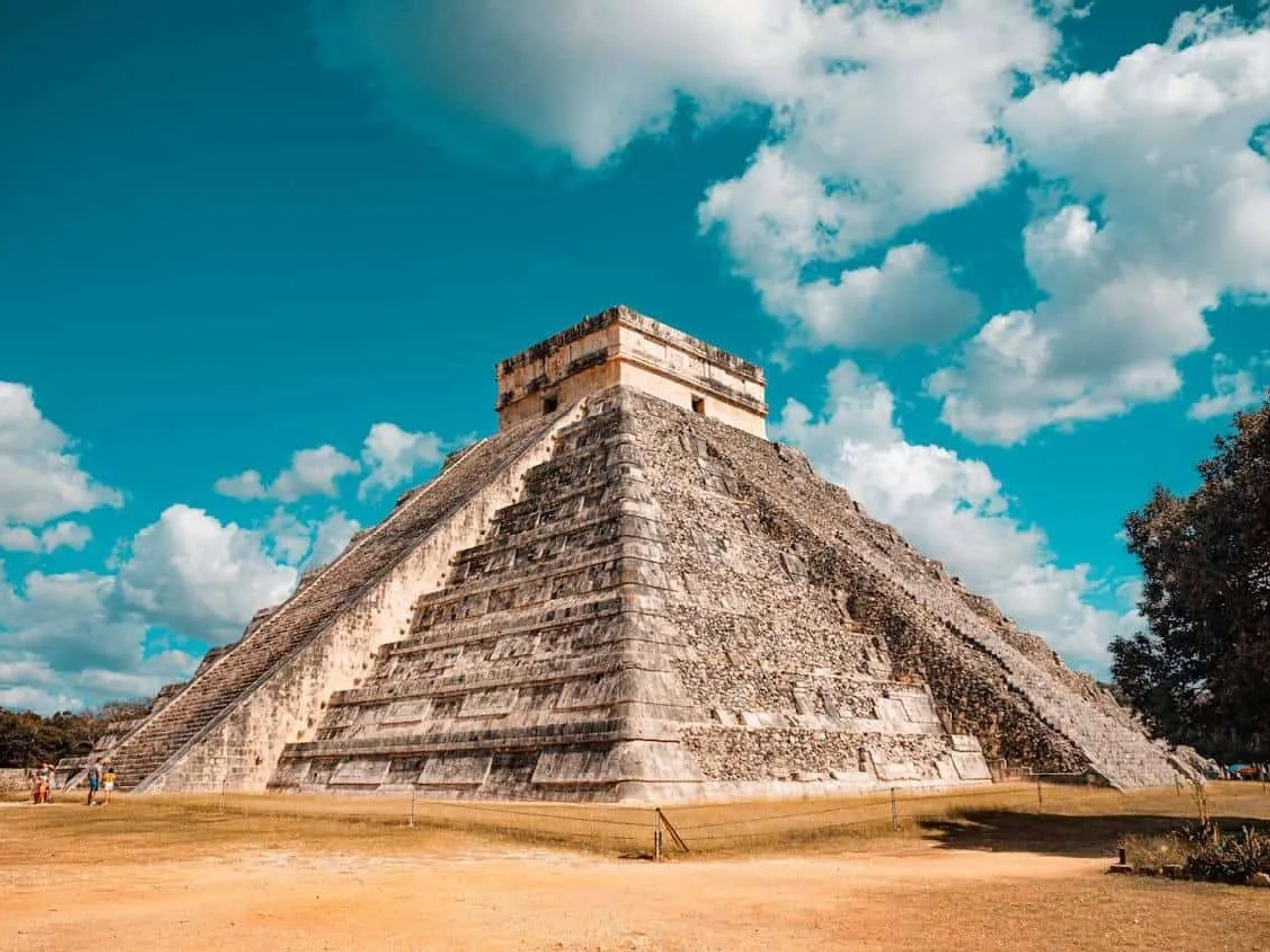 Pirâmide de Chichén Itzá sob céu azul, com visitantes ao redor.
