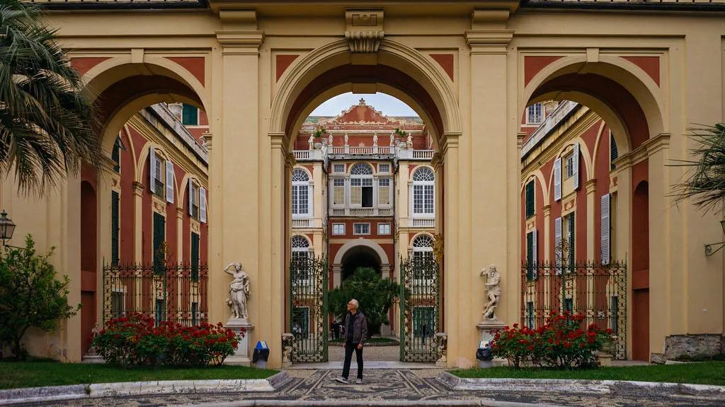 Arcos imponentes em um palácio histórico com jardins e estátuas.