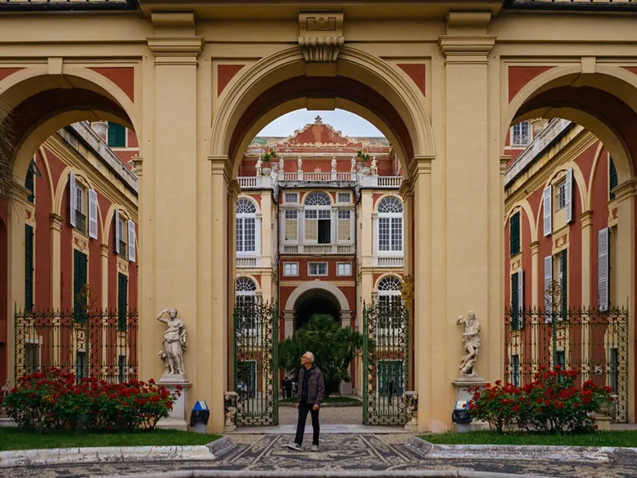 Arcos imponentes em um palácio histórico com jardins e estátuas.