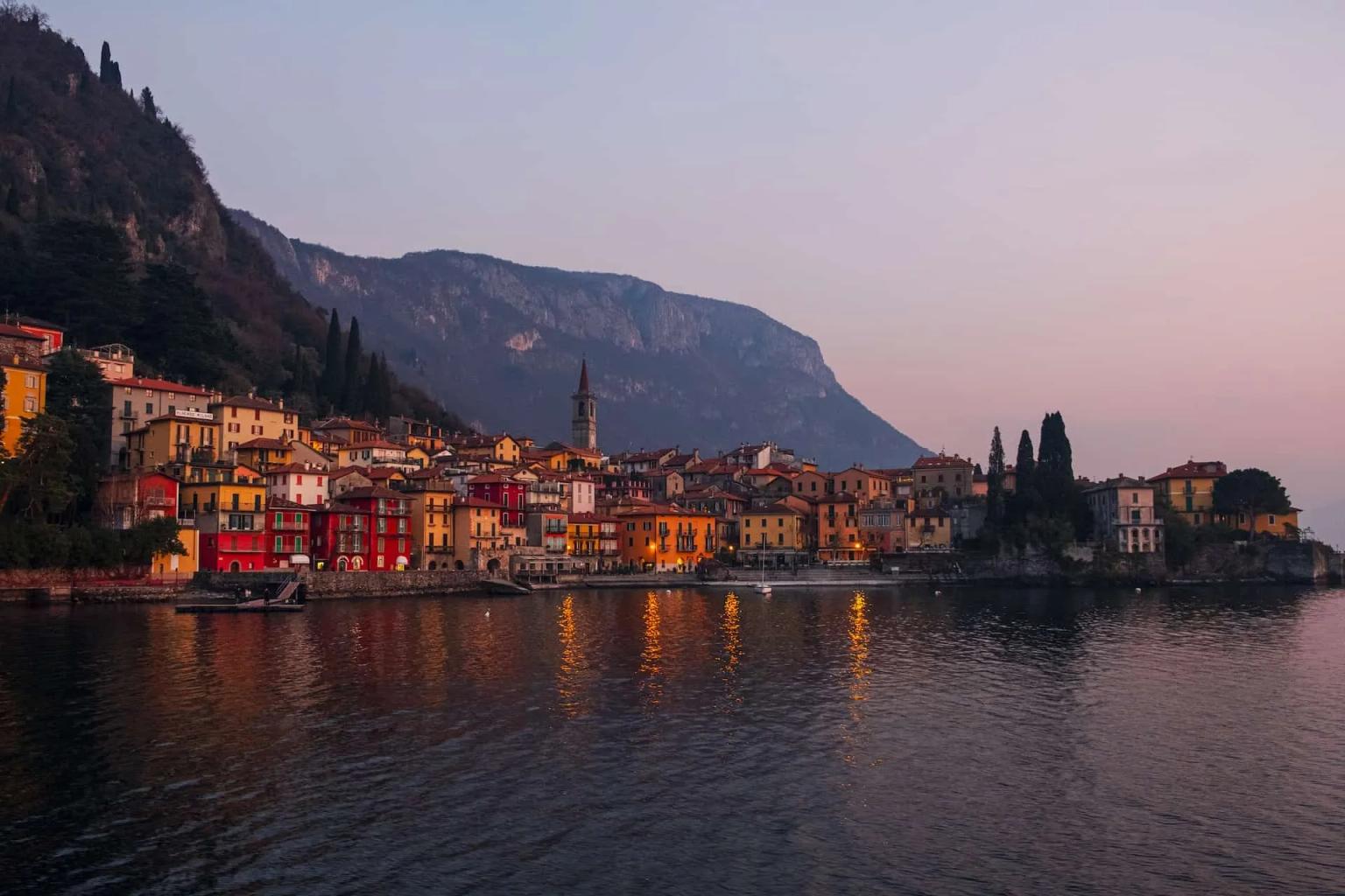 Vista do lago com casas coloridas e montanhas ao fundo ao amanhecer.