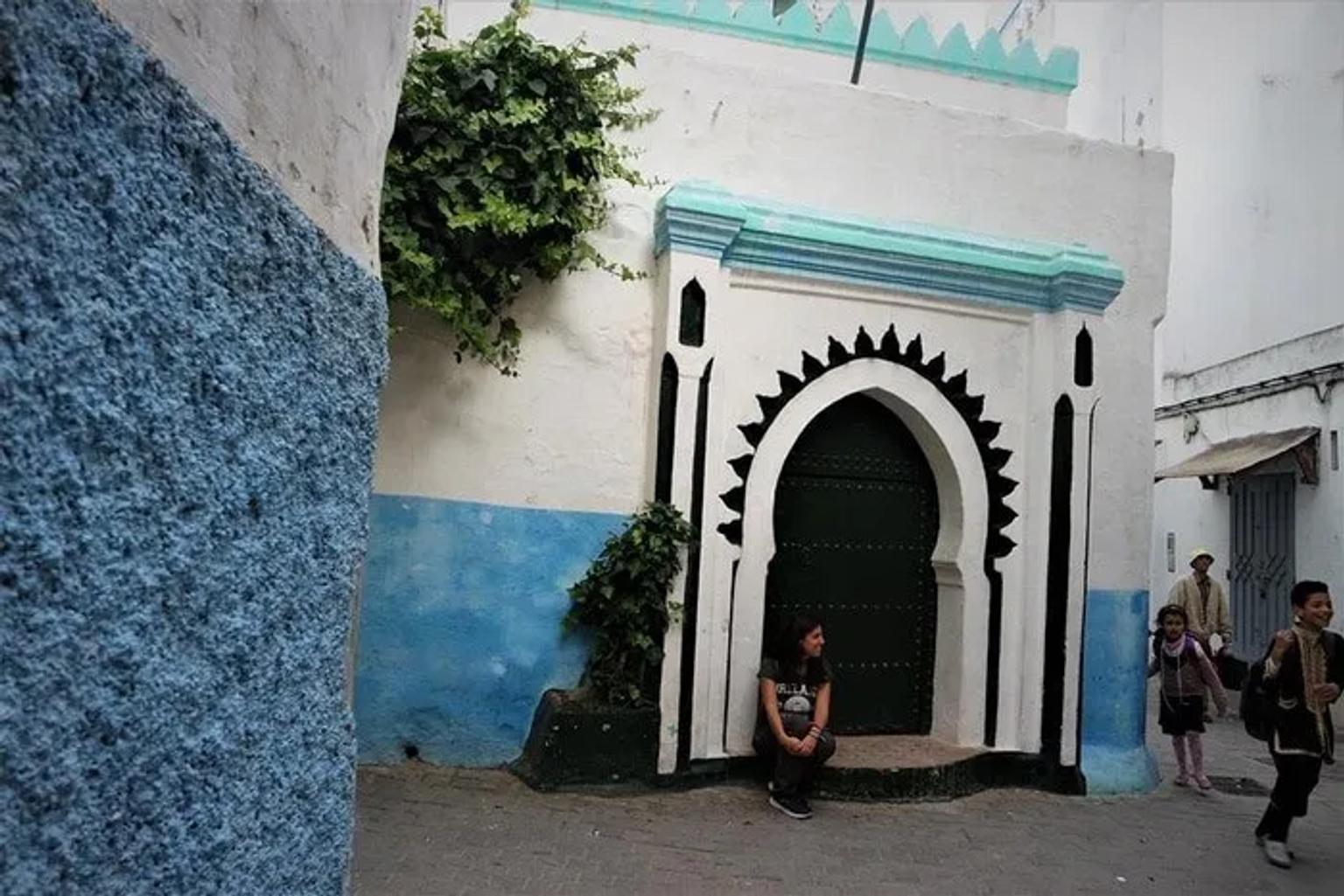 Una joven sentada junto a una puerta decorativa en una calle colorida.