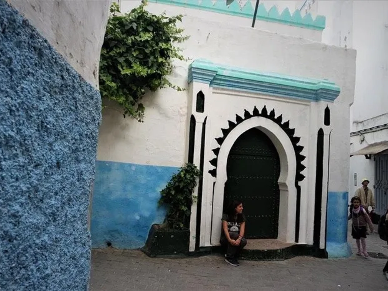 Una joven sentada junto a una puerta decorativa en una calle colorida.