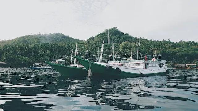 Barcos ancorados em águas calmas, cercados por vegetação tropical no Sudeste Asiático.