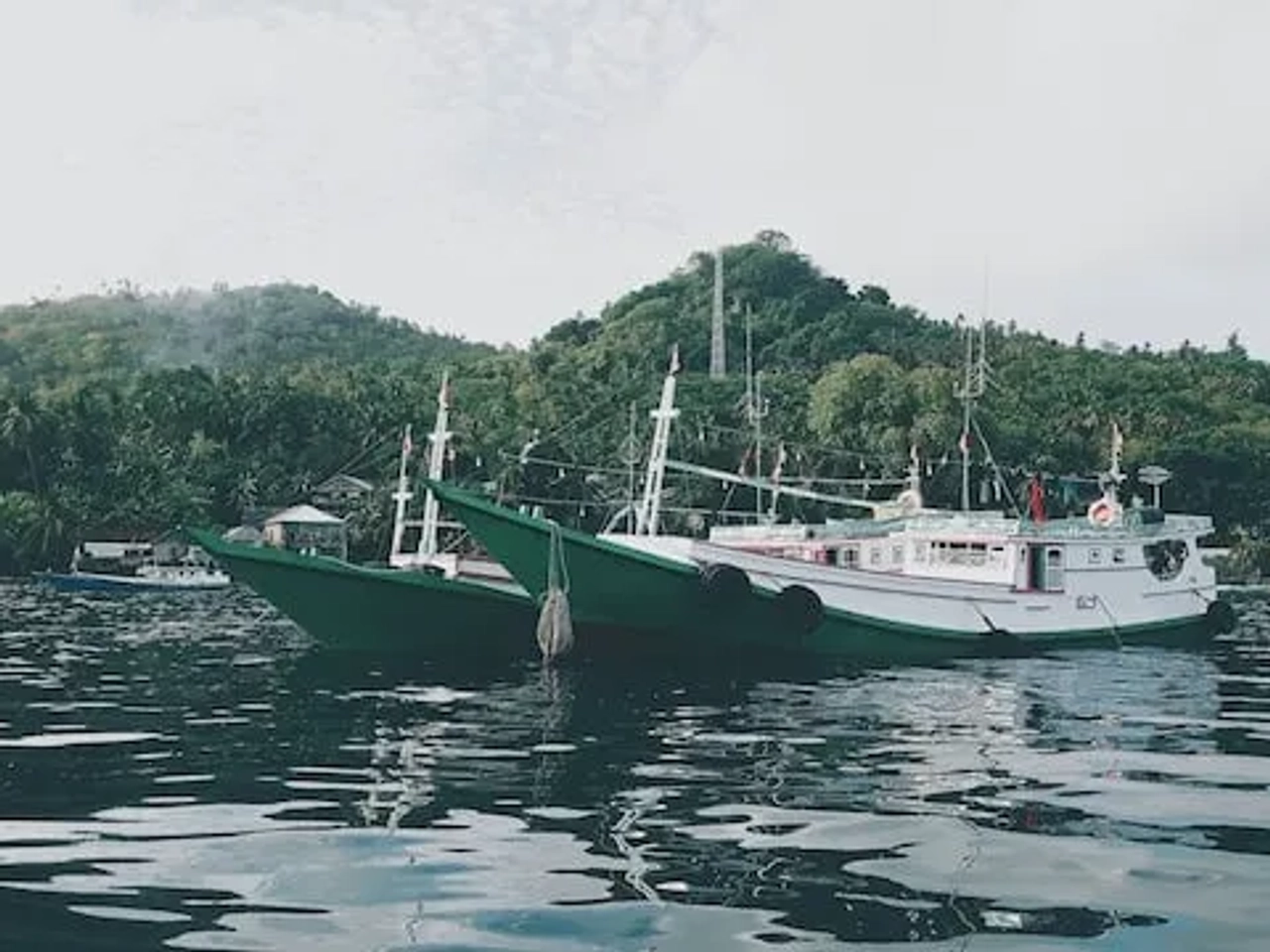 Barcos ancorados em águas calmas, cercados por vegetação tropical no Sudeste Asiático.