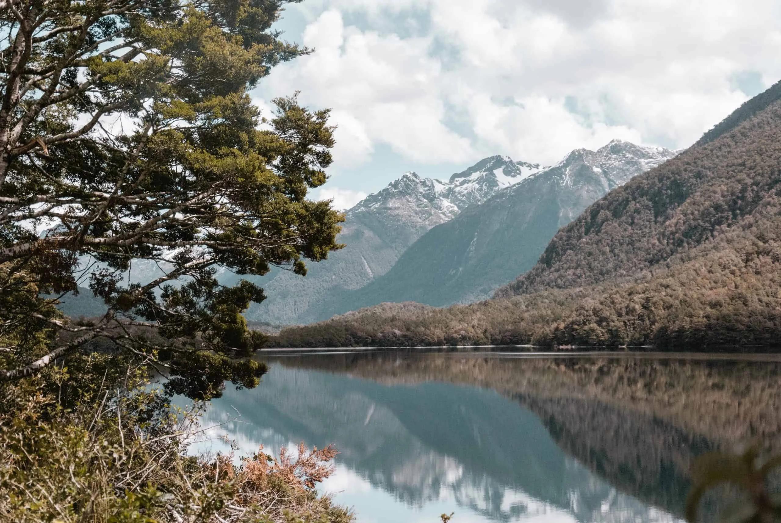 Paisagem montanhosa com lago refletindo, representando a beleza natural da Nova Zelândia.