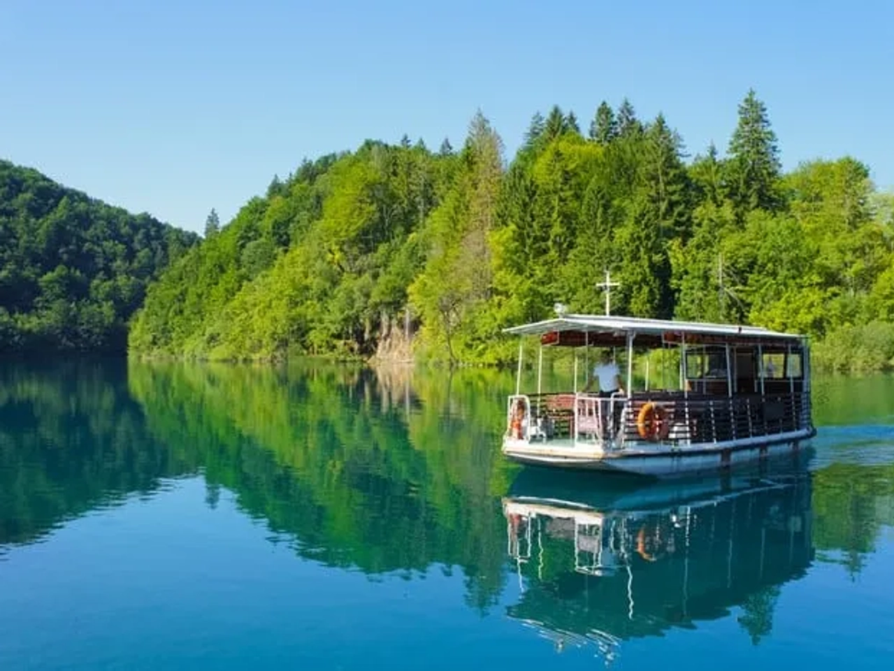 Barco navegando en un lago rodeado de vegetación en un parque nacional de Croacia.