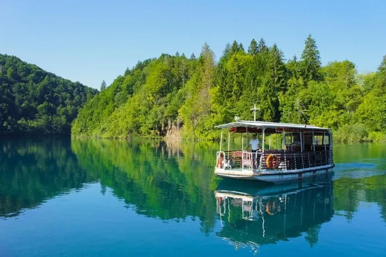 Barco navegando en un lago rodeado de vegetación en un parque nacional de Croacia.