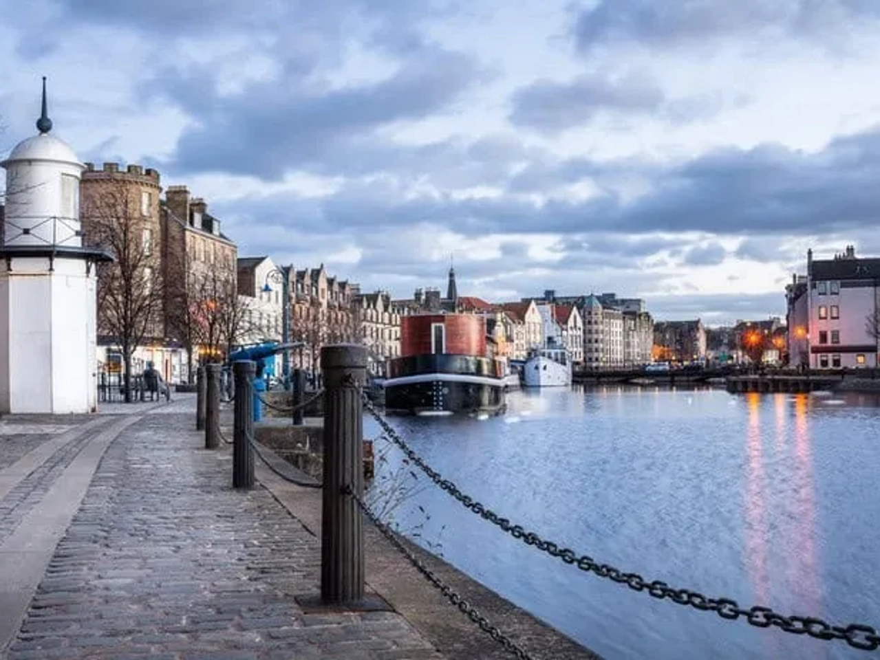 Vista do canal em Edimburgo, com edifícios históricos e céu nublado ao fundo.