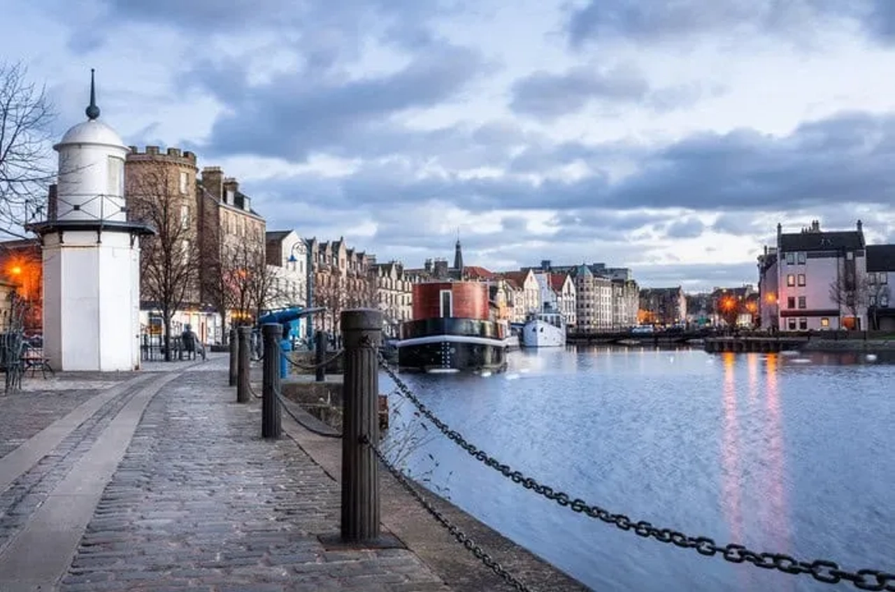Vista do canal em Edimburgo, com edifícios históricos e céu nublado ao fundo.