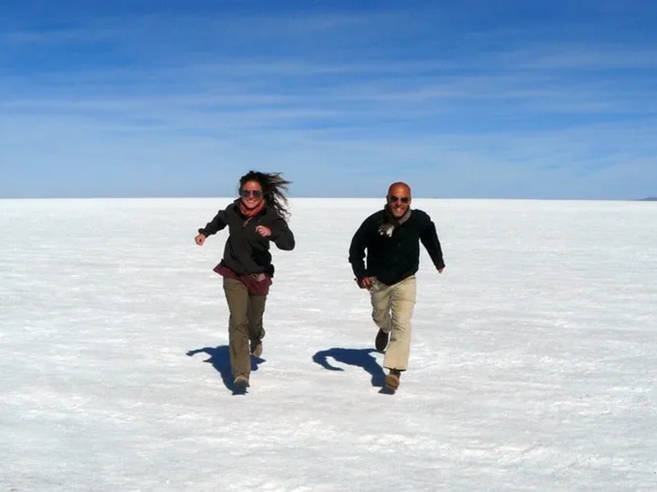 Dos personas corriendo sobre un paisaje de sal bajo un cielo azul.