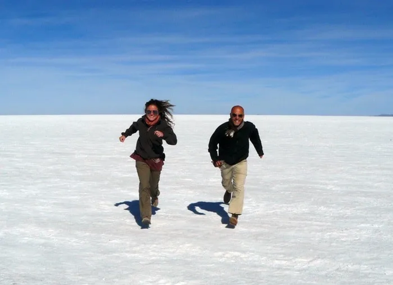 Dos personas corriendo sobre un paisaje de sal bajo un cielo azul.