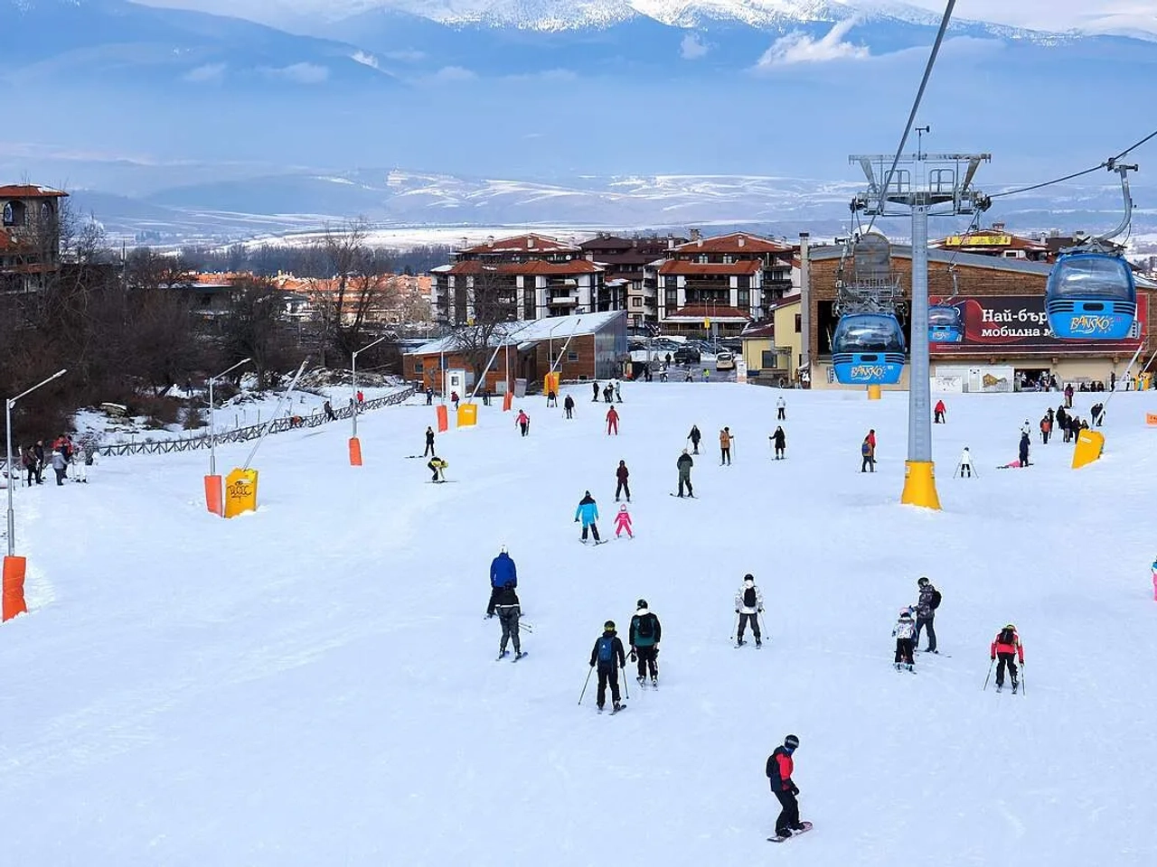 Pista de esqui movimentada com esquiadores e teleféricos ao fundo.