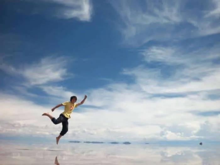 Niño corriendo en un paisaje reflejante bajo un cielo azul con nubes.