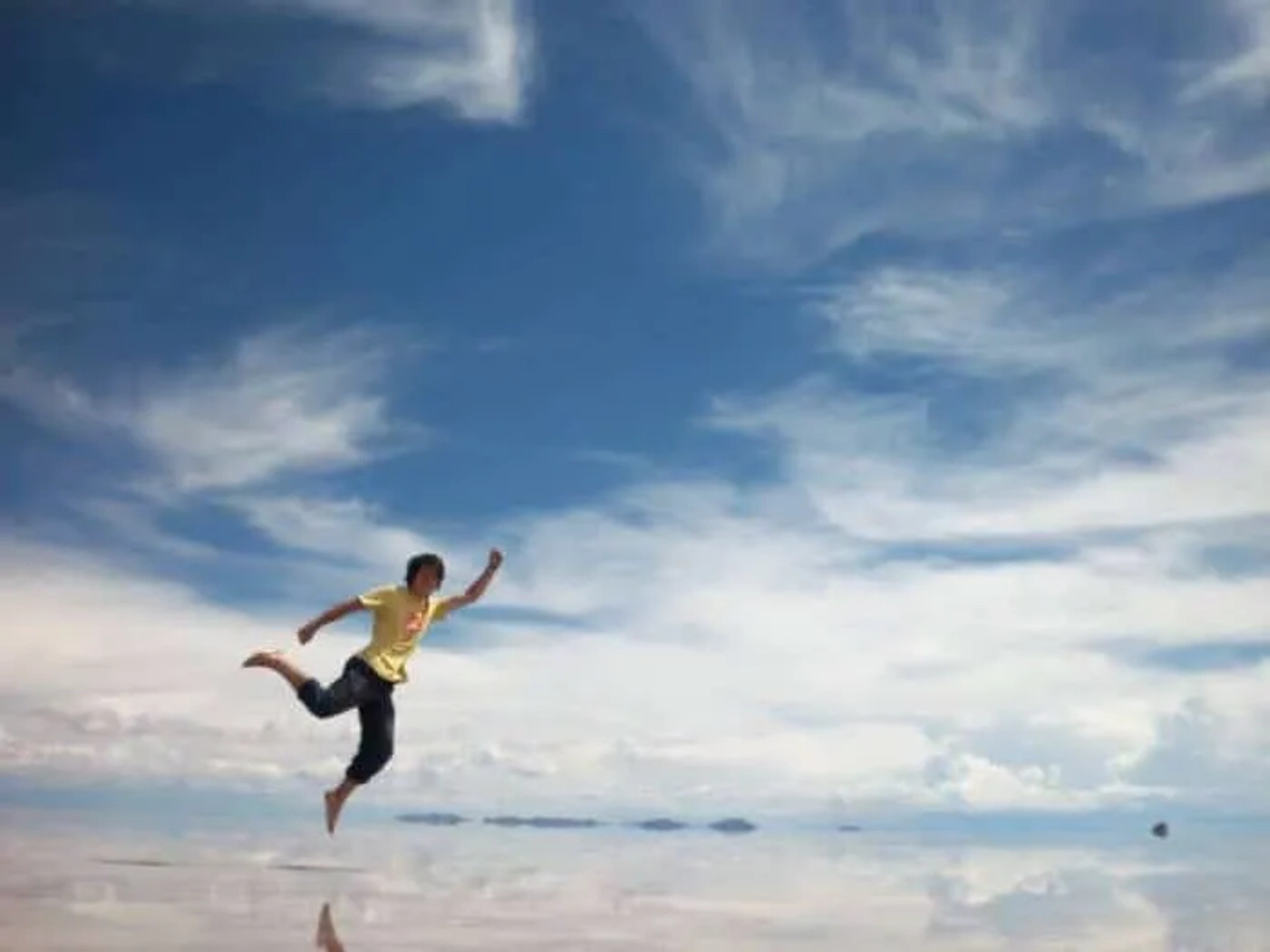 Niño corriendo en un paisaje reflejante bajo un cielo azul con nubes.
