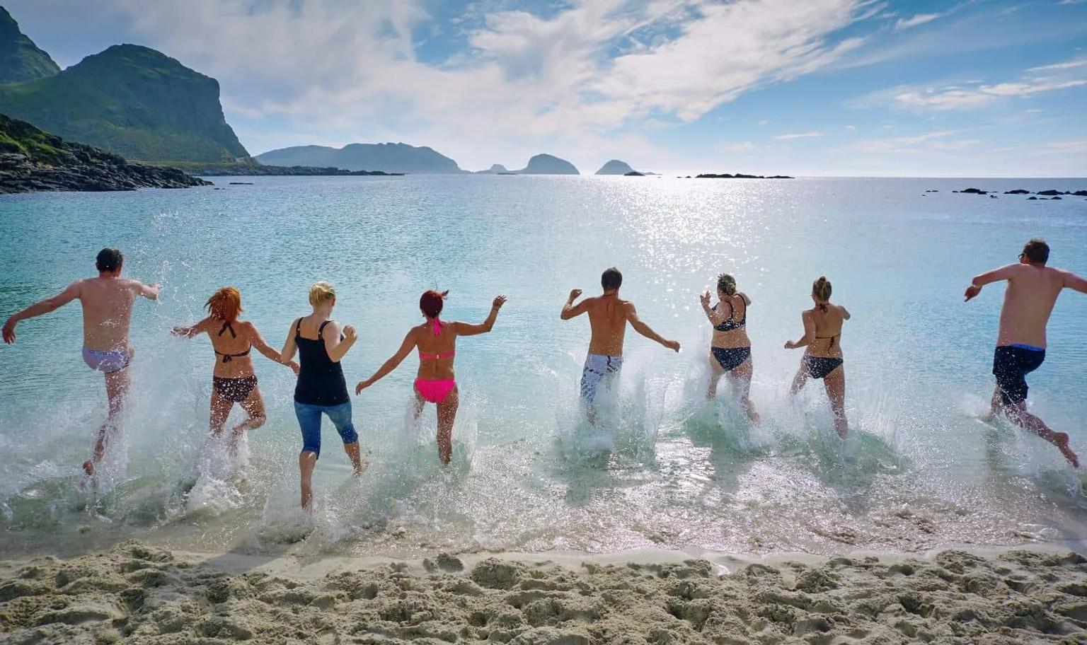 Grupo de pessoas se divertindo na água em uma praia ensolarada.