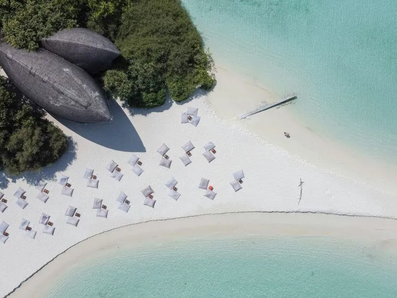 Playa de arena blanca con tumbonas y un barco en la costa de Maldivas.