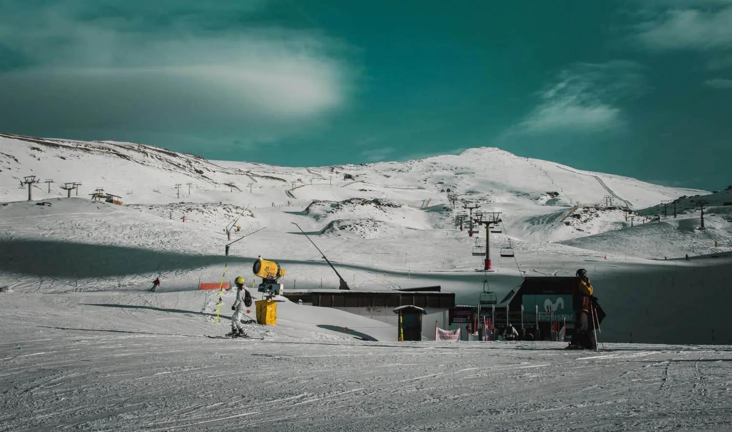 Estação de esqui com neve, teleféricos e montanhas ao fundo.