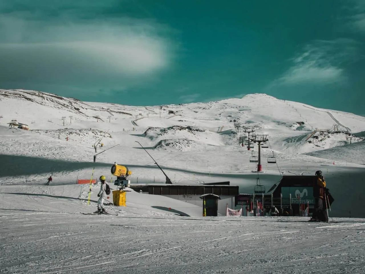 Estação de esqui com neve, teleféricos e montanhas ao fundo.