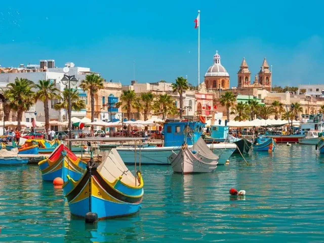 Puerto de Malta con coloridos barcos y edificios históricos al fondo.