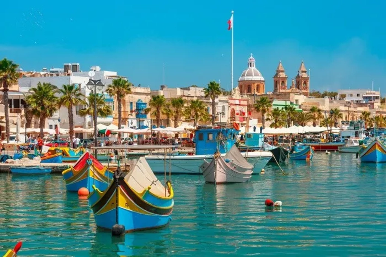 Puerto de Malta con coloridos barcos y edificios históricos al fondo.