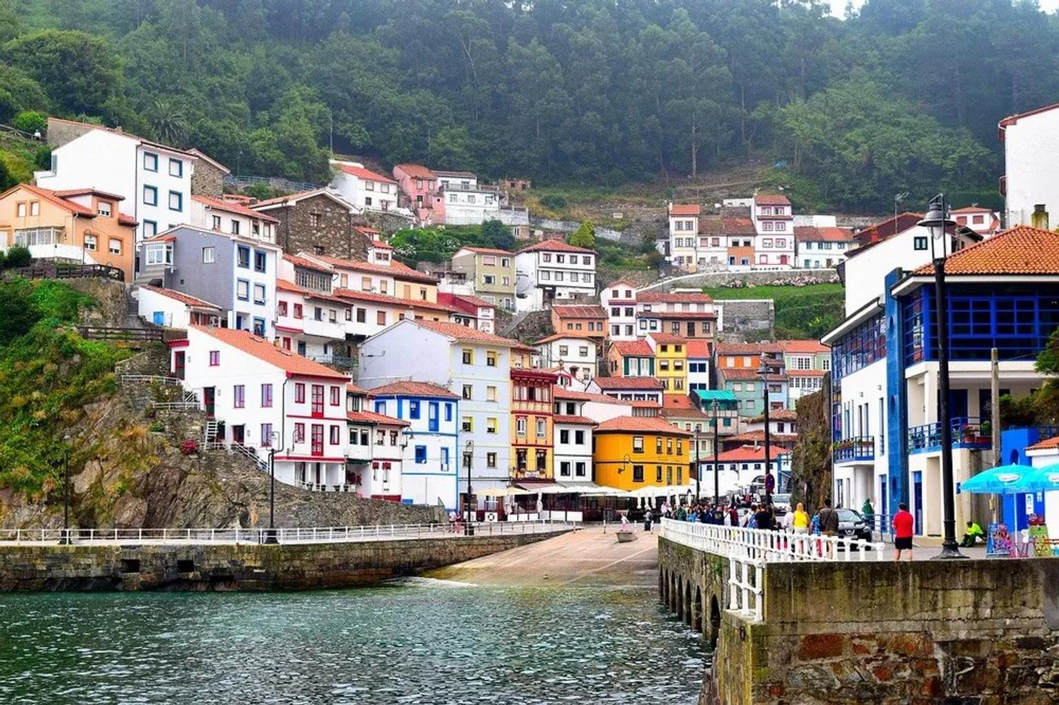 Vista de casas coloridas à beira-mar nas Astúrias, com pessoas caminhando.