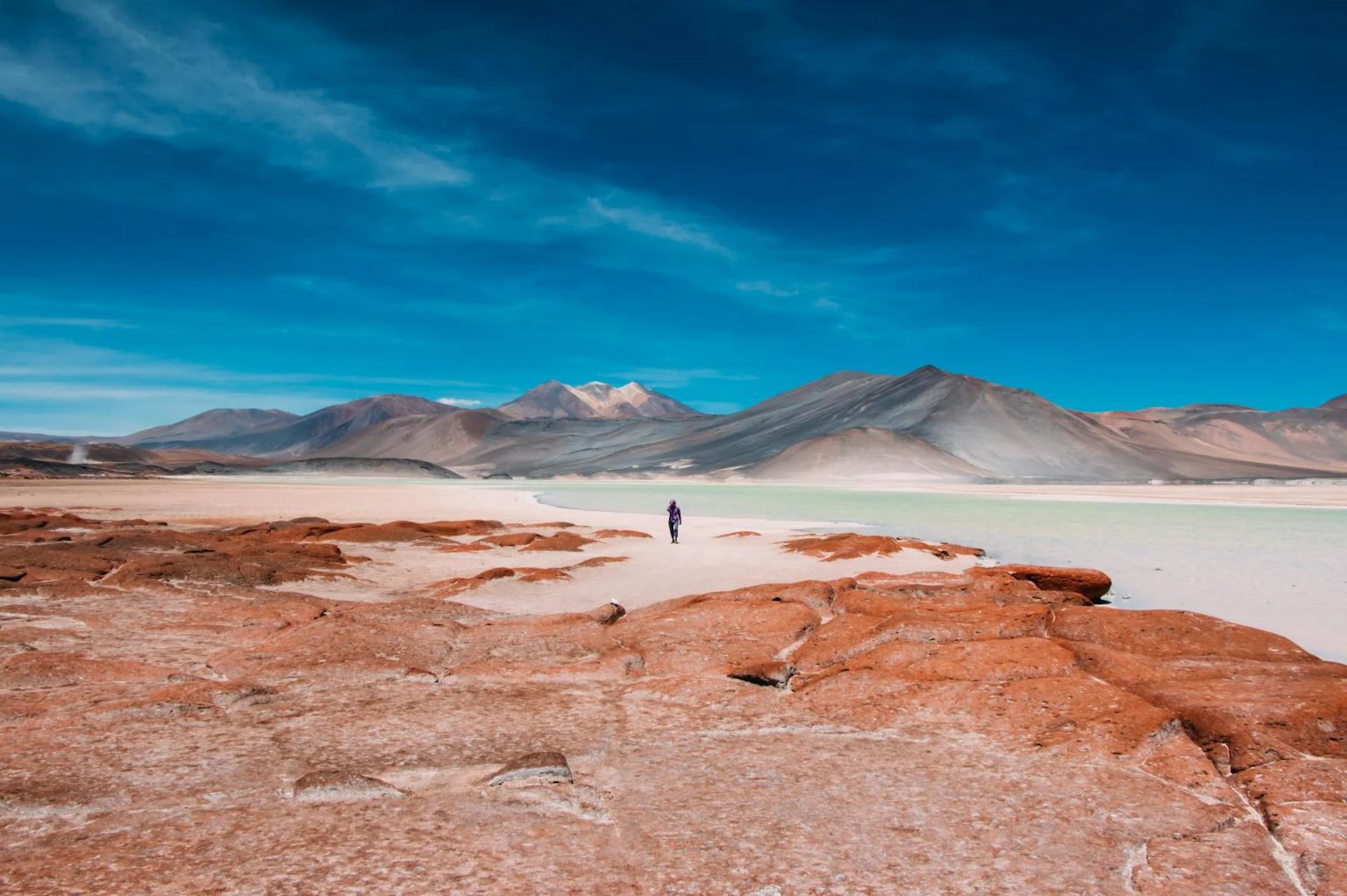 Paisagem desértica do Chile com montanhas ao fundo e uma pessoa caminhando.