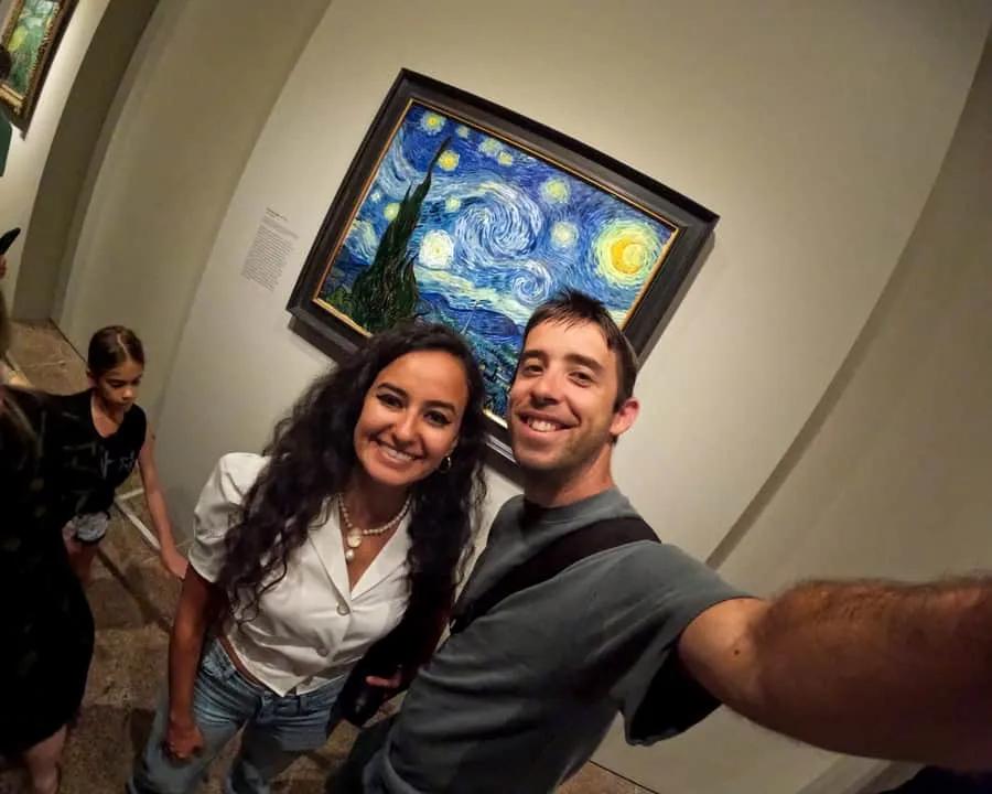 Pareja sonriente en un museo, frente a la pintura "La noche estrellada" de Van Gogh.