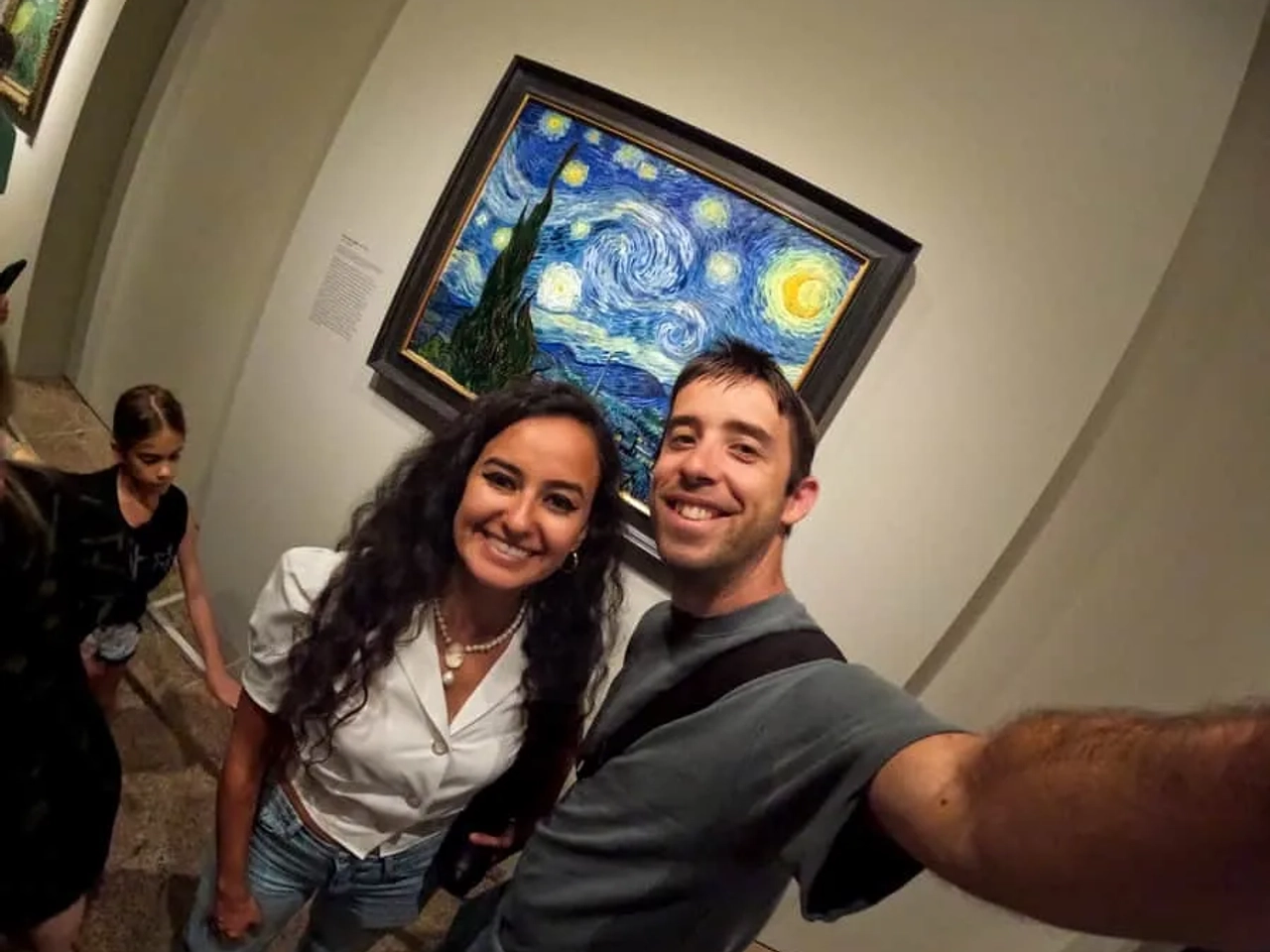 Pareja sonriente en un museo, frente a la pintura "La noche estrellada" de Van Gogh.