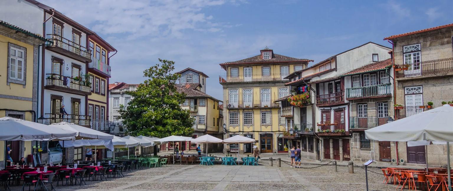 Praça em Guimarães com mesas de restaurantes e edifícios históricos ao fundo.