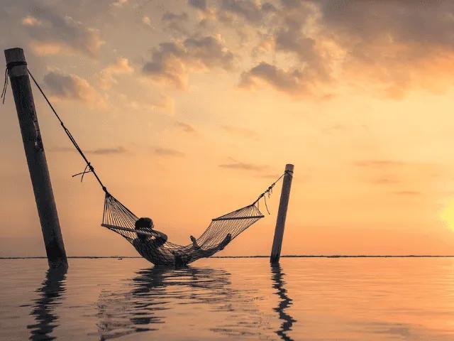 homem deitado numa rede presa em dois paus no meio da agua em bali no sudeste asiatico