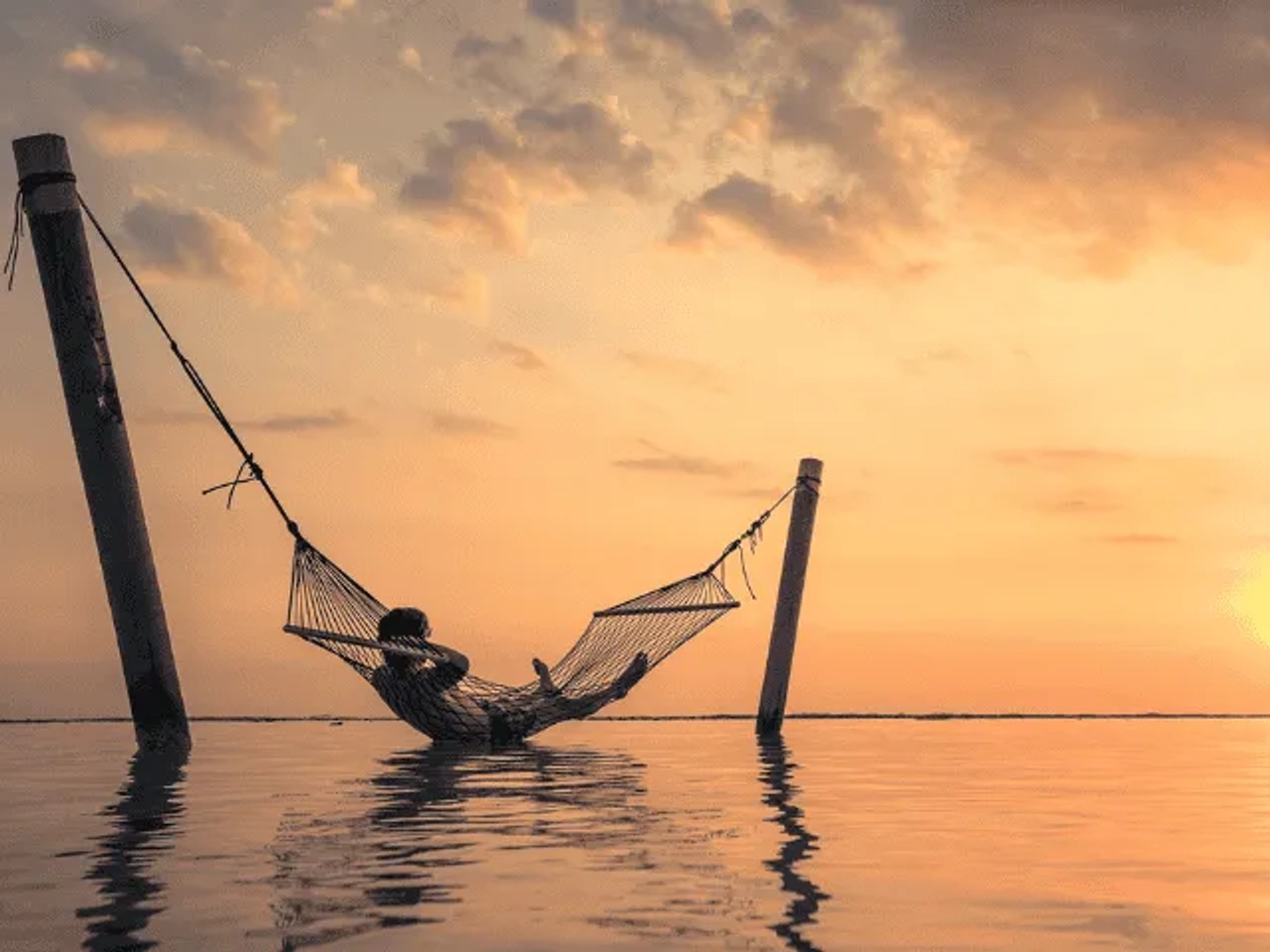 homem deitado numa rede presa em dois paus no meio da agua em bali no sudeste asiatico