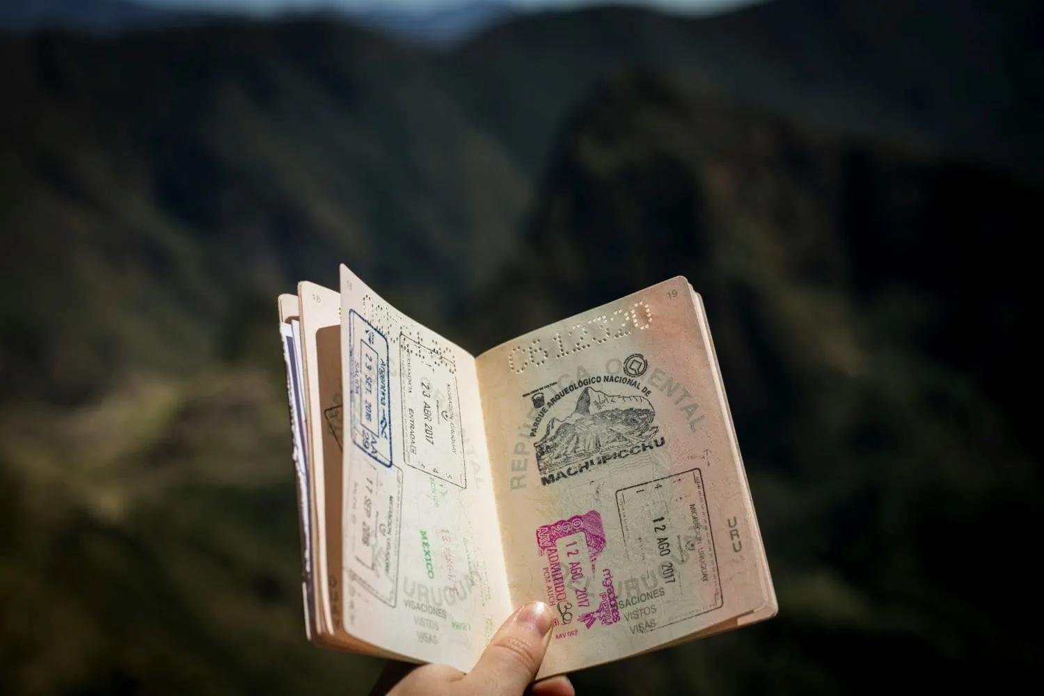 Passaporte aberto com carimbos de viagens, em meio a uma paisagem montanhosa.
