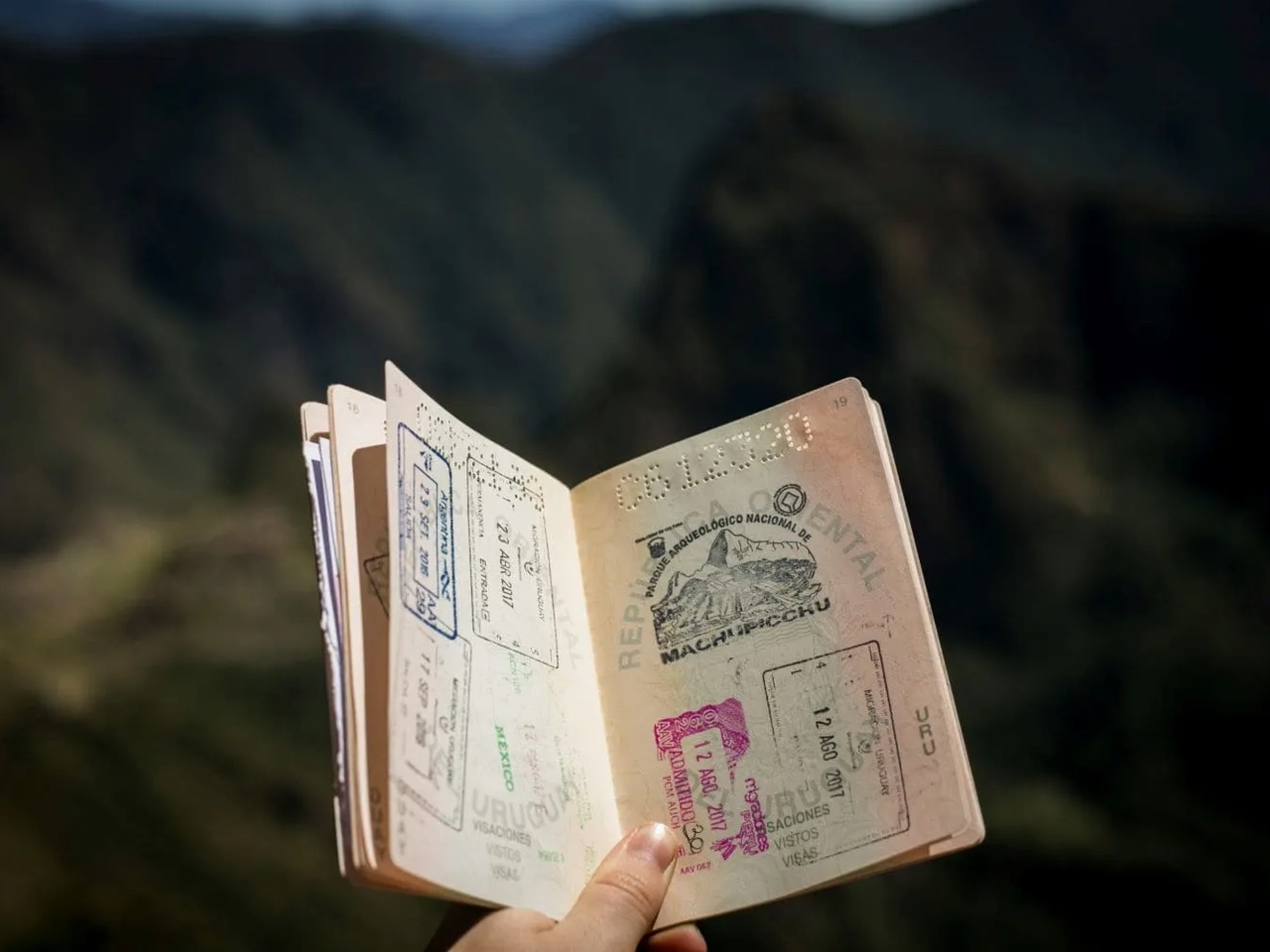 Passaporte aberto com carimbos de viagens, em meio a uma paisagem montanhosa.
