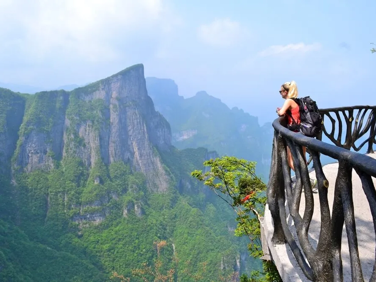 mulher com mochila num miradouro em frente a um vale
