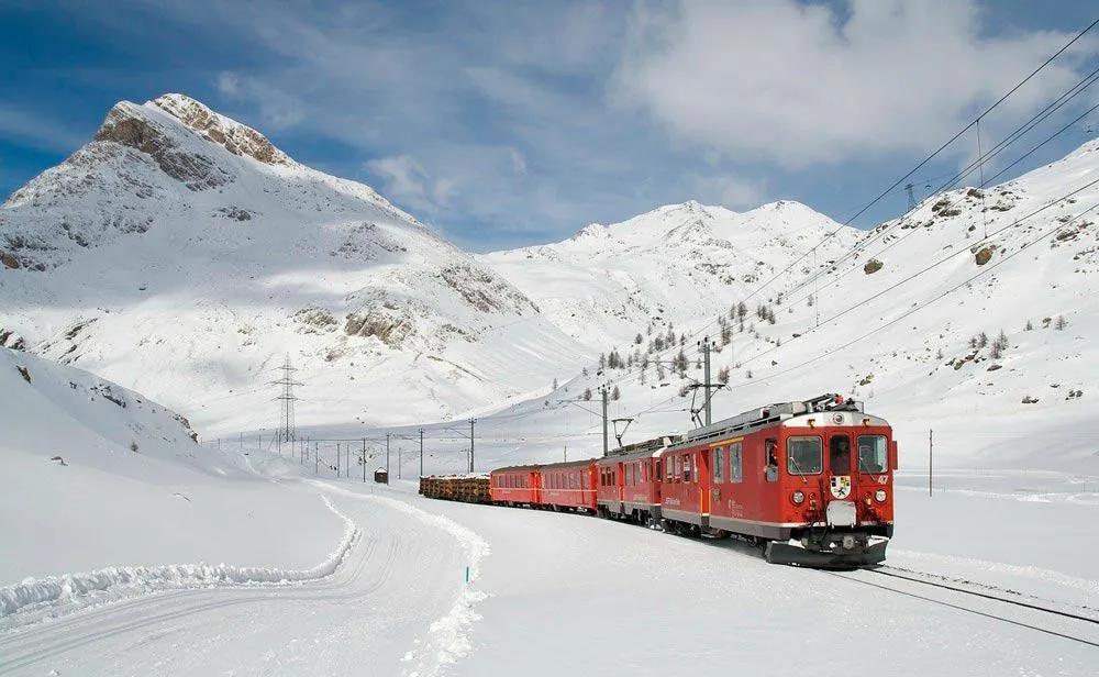 Trem vermelho atravessando paisagem montanhosa coberta de neve na Suíça.