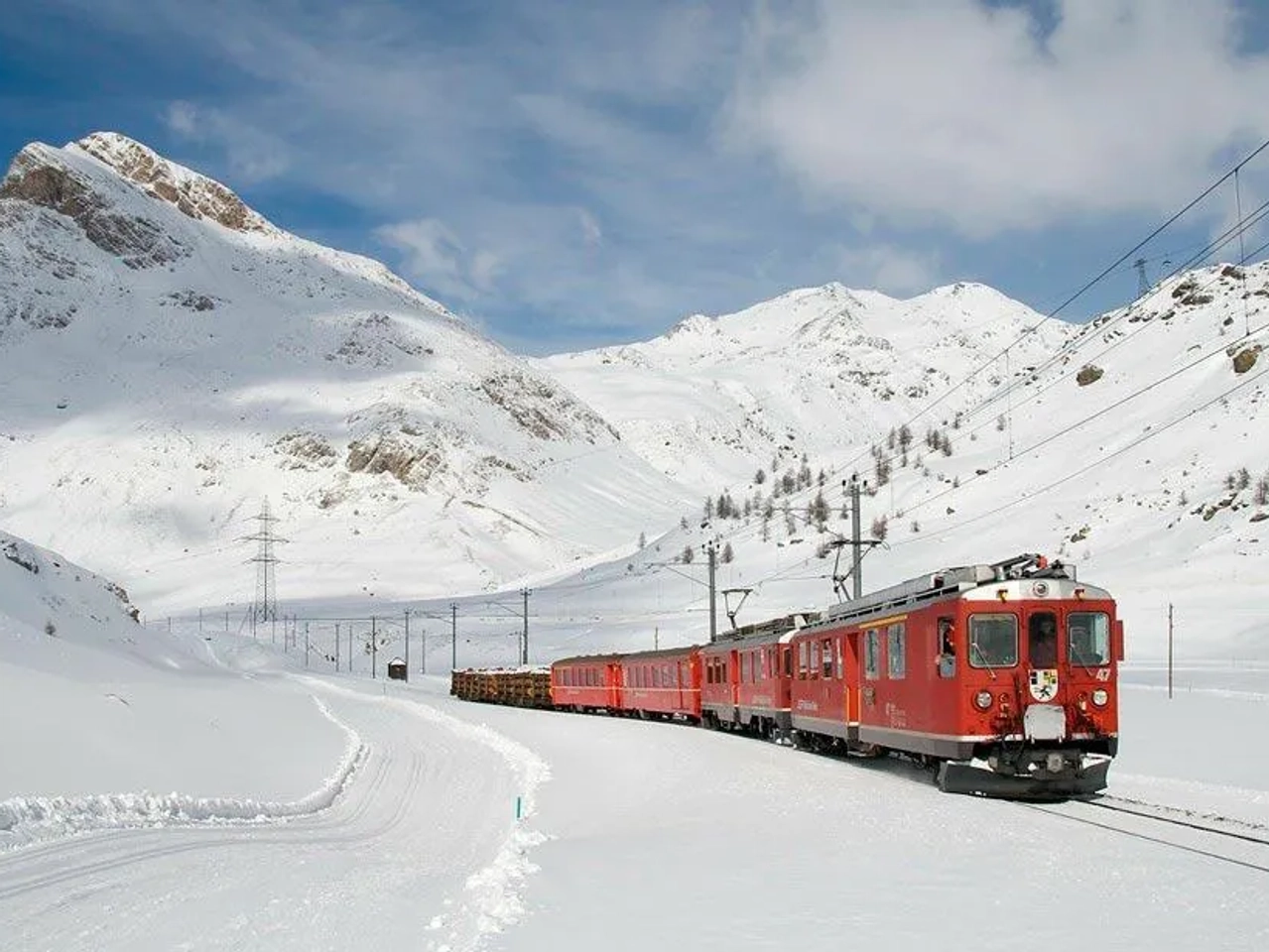 Trem vermelho atravessando paisagem montanhosa coberta de neve na Suíça.