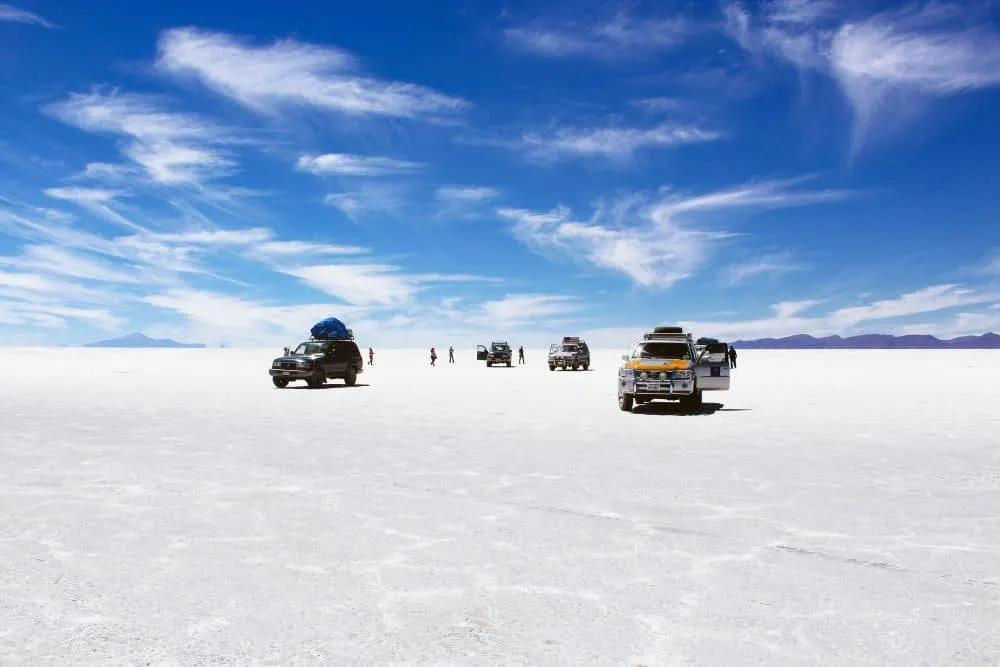 Vehículos en el Salar de Uyuni bajo un cielo despejado y nubes.
