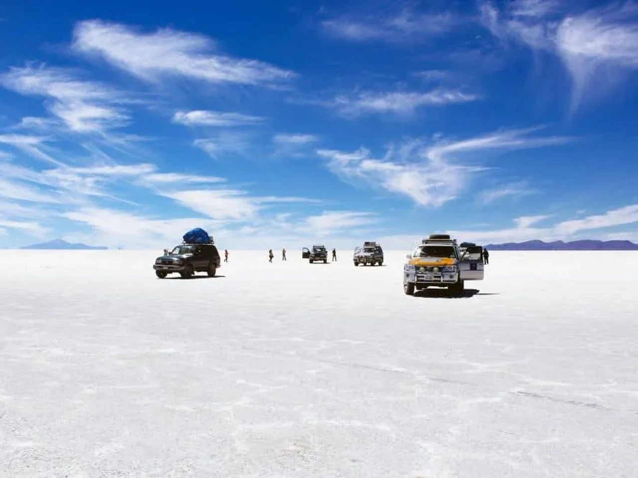 Vehículos en el Salar de Uyuni bajo un cielo despejado y nubes.