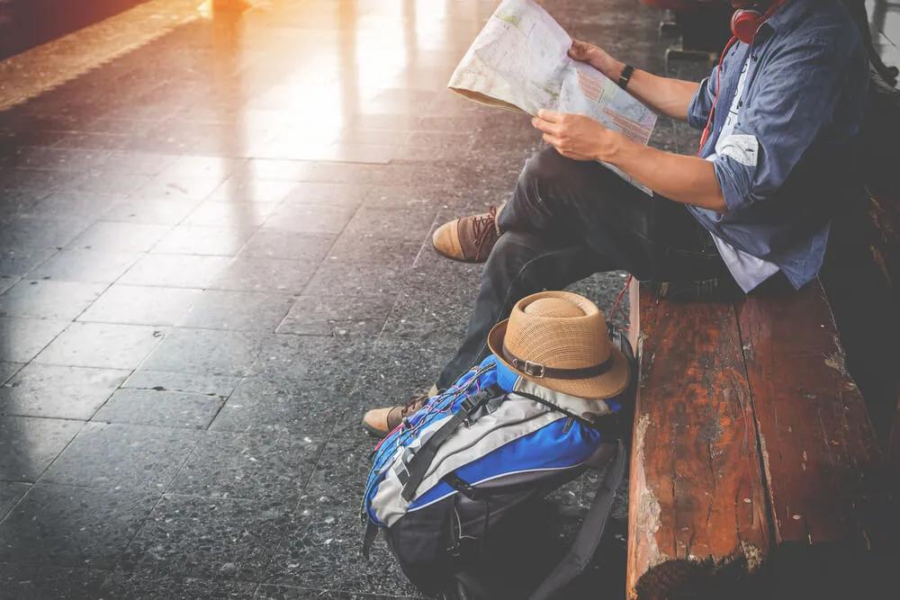 rapaz jovem sentado num banco com mochila ao lado