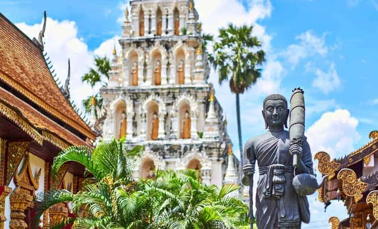 Templo budista na Tailândia com estátua de Buda e torre branca ao fundo.